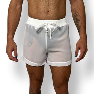 May include: White sheer shorts with a drawstring waist. The shorts have a relaxed fit and are made of a lightweight, semi-transparent fabric. The waistband is solid white, and the shorts have a simple, minimalist design.