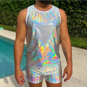 May include: A sleeveless tank top and matching shorts set made from a reflective, holographic silver fabric that displays a spectrum of iridescent colors. The tank top features a solid white trim around the round neckline and the arm openings.