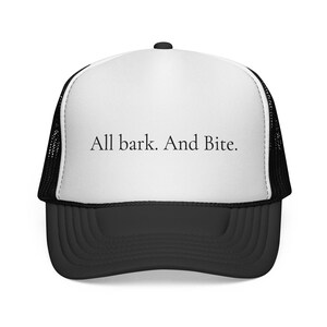 May include: A black and white trucker hat with the text "All bark. And Bite." The hat has a white front panel with the text in black, a black curved brim, and a black mesh back.