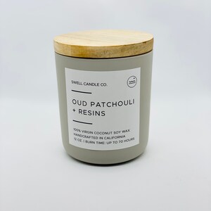 Puede incluir: Un tarro de vela gris con una tapa de madera. La etiqueta dice "SWELL CANDLE CO. OUD PATCHOULI + RESINS 100% VIRGIN COCONUT SOY WAX HANDCRAFTED IN CALIFORNIA 12 OZ. I BURN TIME: UP TO 70 HOURS"