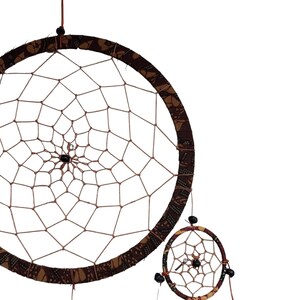 May include: A brown and tan dreamcatcher with a beaded fringe. The dreamcatcher has a circular frame with a web-like pattern and a smaller dreamcatcher hanging below it.