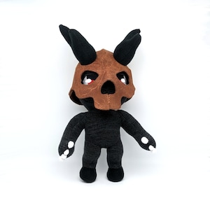 May include: Black plush toy with a brown skull helmet. The toy has white claws and red eyes.