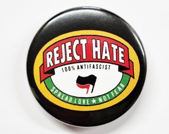 Könnte beinhalten: Schwarzer und gelber Knopf mit dem Text "Reject Hate 100% Anti-Fascist" in einem roten Banner. Der Knopf hat auch ein schwarzes und rotes Anarchiesymbol und den Text "Spread Love Not Fear" in einem grünen Banner.