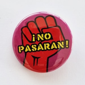 Puede incluir: Un puño rojo con fondo amarillo y el texto "NO PASARAN!" en un botón rosa.