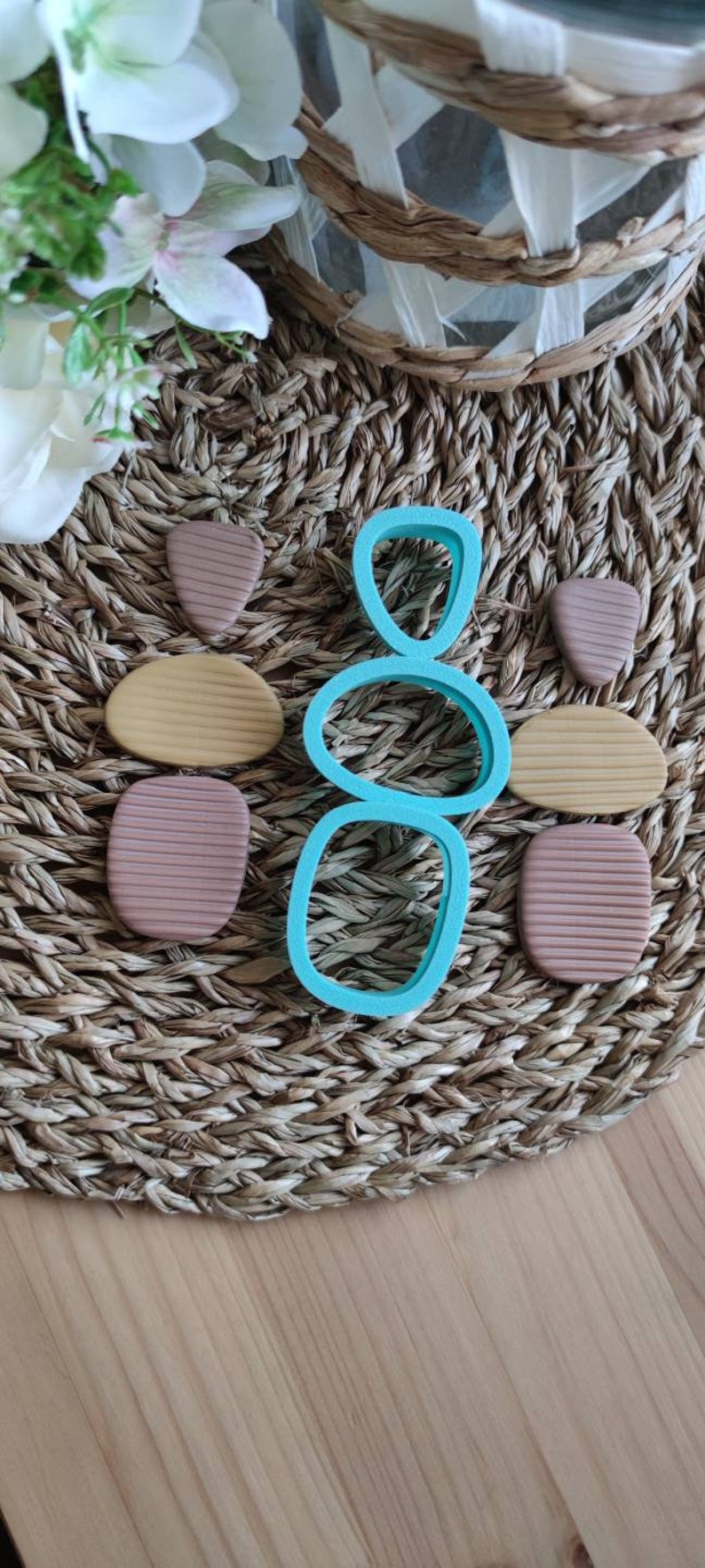 Op de afbeelding: Een set teal plastic koekjesvormen in de vorm van gestapelde stenen. De vormen liggen op een geweven bruine mat met bruine, beige en beige klei vormen.