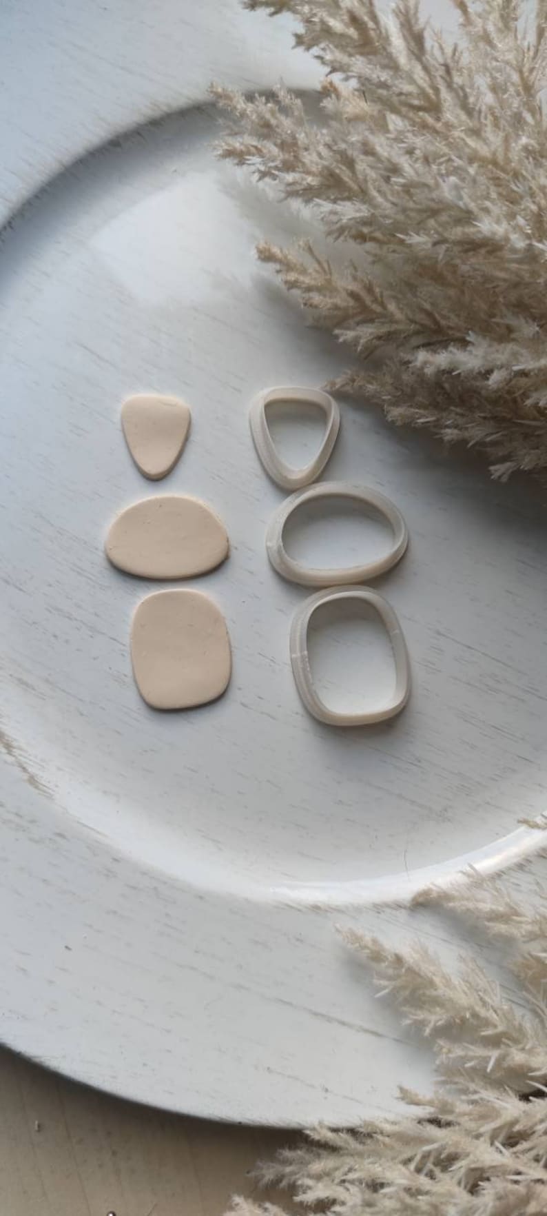 Op de afbeelding: Een set van vier polymer clay cutters in de vorm van abstracte organische vormen. De cutters zijn wit en zijn gerangschikt op een wit oppervlak. Er zijn drie beige polymer clay vormen naast de cutters.
