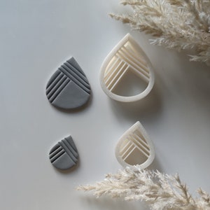Könnte beinhalten: Ein Set mit drei tropfenförmigen Polymer Clay Cuttern. Zwei Cutter sind weiß und einer ist grau. Die Cutter haben ein geometrisches Design mit Linien.