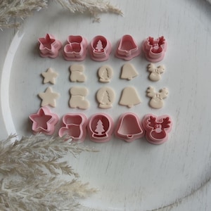 Könnte beinhalten: Ein Set mit 12 rosafarbenen Weihnachts-Ausstechern aus Kunststoff. Die Ausstecher haben die Form eines Sterns, eines Stiefels, einer Schneekugel, einer Glocke und eines Rentiers.