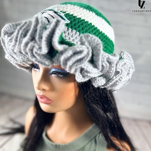 May include: A handmade crochet hat with a gray ruffled brim and a striped crown in green and white. The hat has a unique design and is perfect for adding a touch of style to any outfit. The hat is a fashionable accessory.