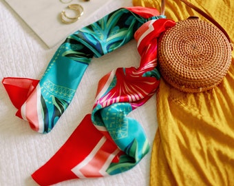 Könnte beinhalten: Ein gelbes Sommerkleid mit einer braunen geflochtenen Tasche, einem rot-blauen gemusterten Schal, einem weißen Hut und einer goldenen Halskette und Uhr auf einer weißen Oberfläche.