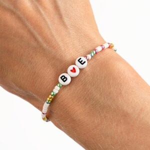 May include: A white beaded bracelet with colourful beads and white letter beads spelling "B ♥ E".
