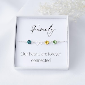 May include: A silver bracelet with four colourful crystals and two silver heart charms. The bracelet comes in a white box with the words "Family Our hearts are forever connected."