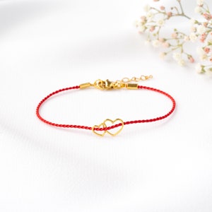 May include: A red string bracelet with a gold double heart charm.