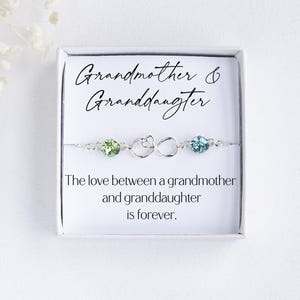 May include: A silver bracelet with green and blue crystals and an infinity symbol charm. The bracelet comes in a white box with the text "Grandmother & Granddaughter. The love between a grandmother and granddaughter is forever."