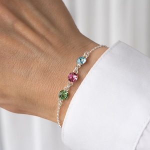 May include: A silver chain bracelet with four round crystals. The crystals are green, pink, and blue.