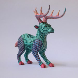 May include: A teal and purple wooden deer figurine with intricate geometric patterns and pink antlers. The deer is standing on a white surface.