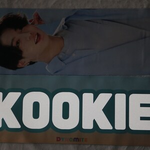 May include: A blue and white banner with the word "KOOKIE" in white letters on a teal background. The banner also has a small yellow star and the word "Dynamite" in white letters on a blue background.