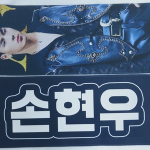 May include: A blue and black fabric banner with white text that reads "MONSTA X" and "Shownu". The banner also has a white number "920618" printed on the right side.