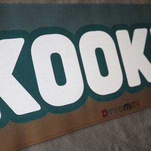 May include: White text on a teal background reads "KOOKIE" with a smaller rainbow text reading "DYNAMITE" below.