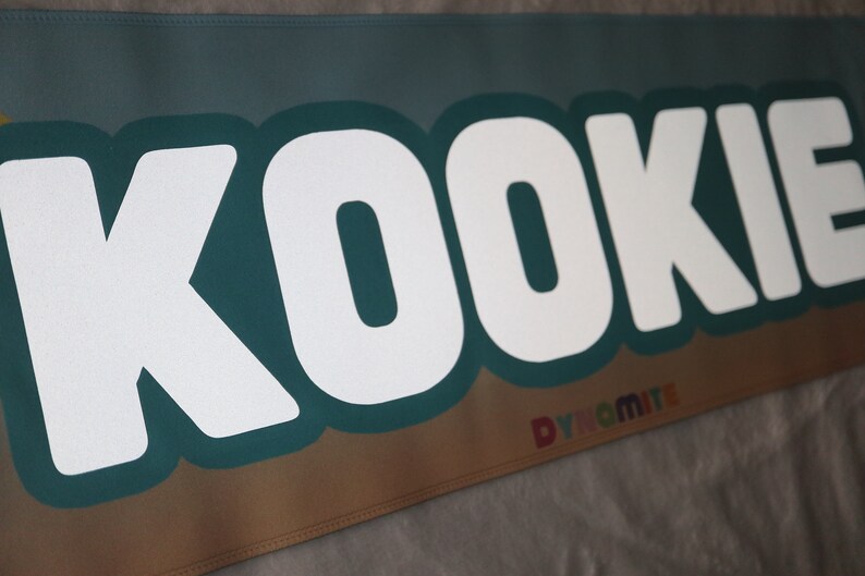 May include: White text on a teal background reads "KOOKIE" with a smaller rainbow text reading "DYNAMITE" below.