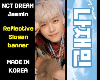 Puede incluir: Bandera de eslogan reflectante con un retrato de Jaemin de NCT DREAM. El anverso muestra la imagen de Jaemin, mientras que el reverso tiene texto coreano sobre un fondo azul. Hecho en Corea.