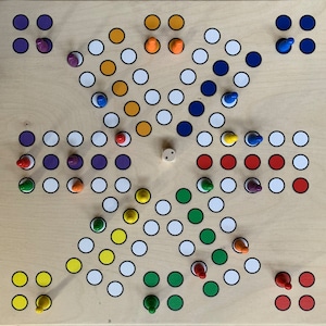 Puede incluir: Un tablero de juego de madera con un patr&oacute;n en forma de estrella de c&iacute;rculos de colores. El tablero tiene un c&iacute;rculo central con un dado de madera. Hay seis piezas de juego de diferentes colores en el tablero: rojo, azul, verde, amarillo, morado y naranja.