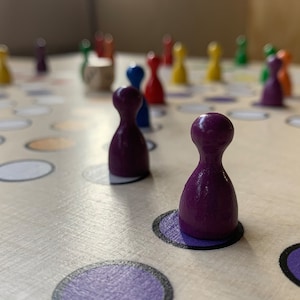 Puede incluir: Piezas de juego moradas en un juego de mesa con c&iacute;rculos blancos y naranjas. Las piezas est&aacute;n hechas de madera y tienen una parte superior redondeada.