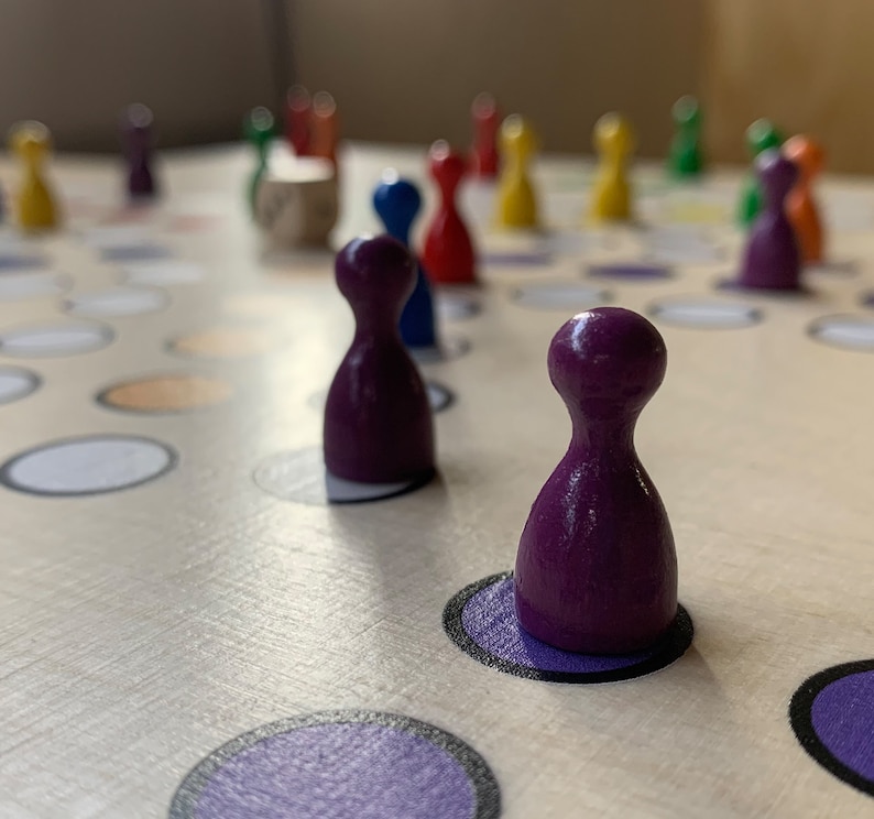 Puede incluir: Piezas de juego moradas en un juego de mesa con c&iacute;rculos blancos y naranjas. Las piezas est&aacute;n hechas de madera y tienen una parte superior redondeada.