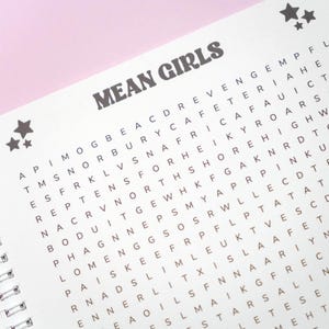 May include: A spiral-bound word search puzzle book with the words "MEAN GIRLS" in bold, dark gray letters at the top. The puzzle grid is filled with letters, and there are star graphics in the upper left corner.
