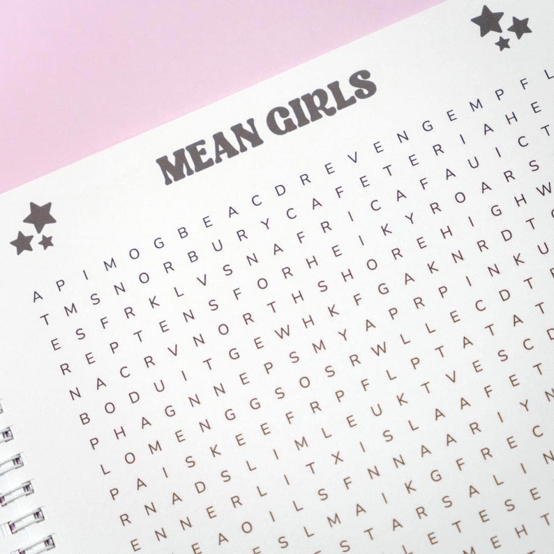 May include: A spiral-bound word search puzzle book with the words "MEAN GIRLS" in bold, dark gray letters at the top. The puzzle grid is filled with letters, and there are star graphics in the upper left corner.
