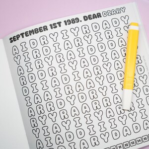 K&ouml;nnte beinhalten: Ge&ouml;ffnete Tagebuchseite mit dem Text "SEPTEMBER 1ST 1989. DEAR DIARY" und einem Buchstabenraster. Ein gelber Textmarker liegt auf der rechten Seite der Seite. Das Tagebuch ist auf einer rosa Oberfl&auml;che ge&ouml;ffnet.