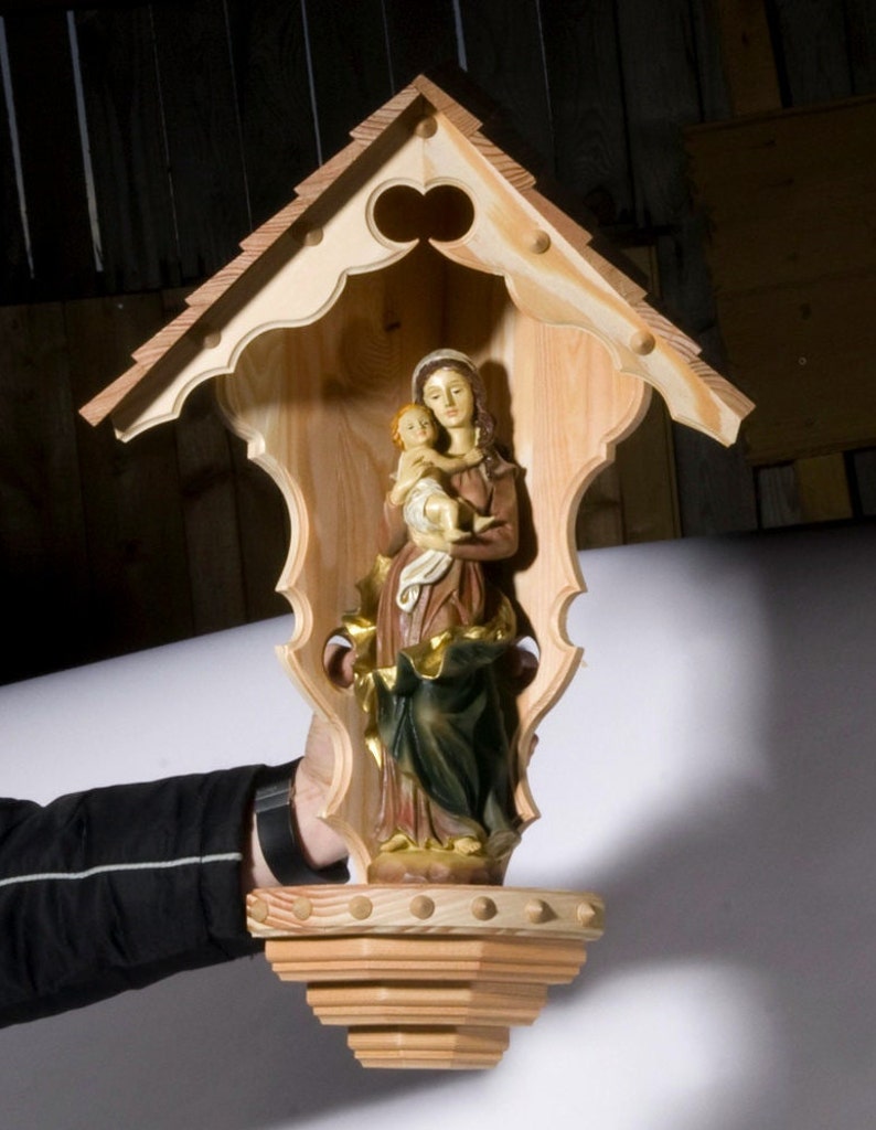 Puede incluir: Un santuario de madera con un techo tallado y una figura de la Virgen Mar&iacute;a sosteniendo a un beb&eacute; Jes&uacute;s en su interior. El santuario est&aacute; pintado en un color madera natural.