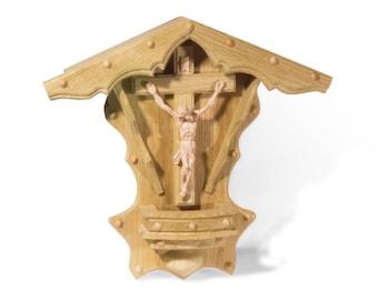 May include: A wooden wall-mounted crucifix with a carved figure of Jesus Christ. The crucifix is surrounded by a decorative wooden frame with a roof-like top.