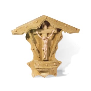 Puede incluir: Un crucifijo de madera para colgar en la pared con una figura tallada de Jesucristo en la cruz. El crucifijo est&aacute; en un marco de madera decorativo con un techo puntiagudo.