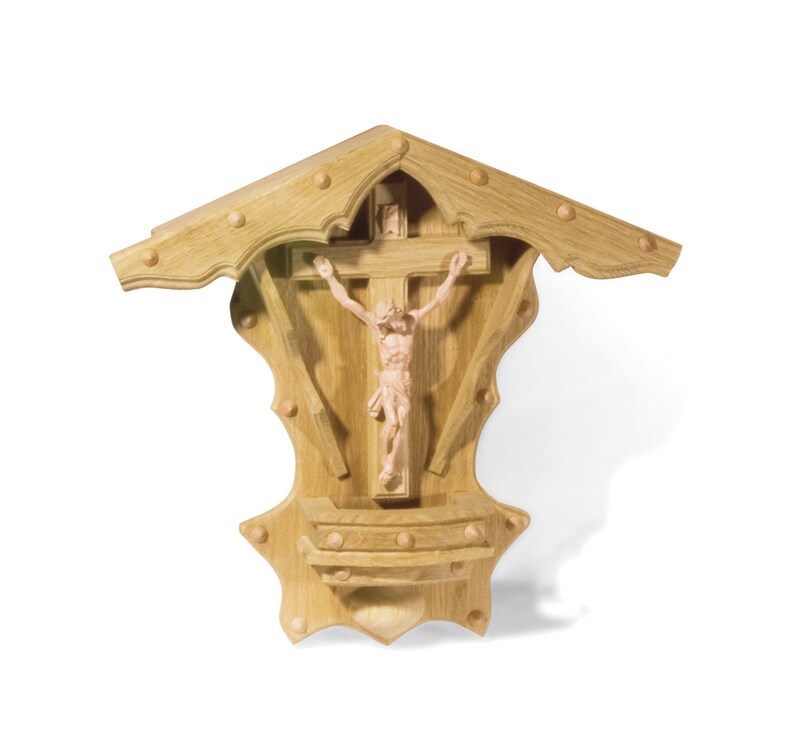 Puede incluir: Un crucifijo de madera para colgar en la pared con una figura tallada de Jesucristo en la cruz. El crucifijo est&aacute; en un marco de madera decorativo con un techo puntiagudo.