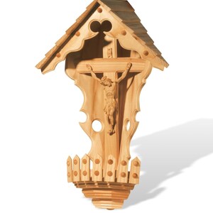 Puede incluir: Un crucifijo de madera para colgar en la pared con una figura tallada de Jesucristo. El crucifijo est&aacute; encerrado en un marco de madera decorativo con un techo y una base en forma de valla.