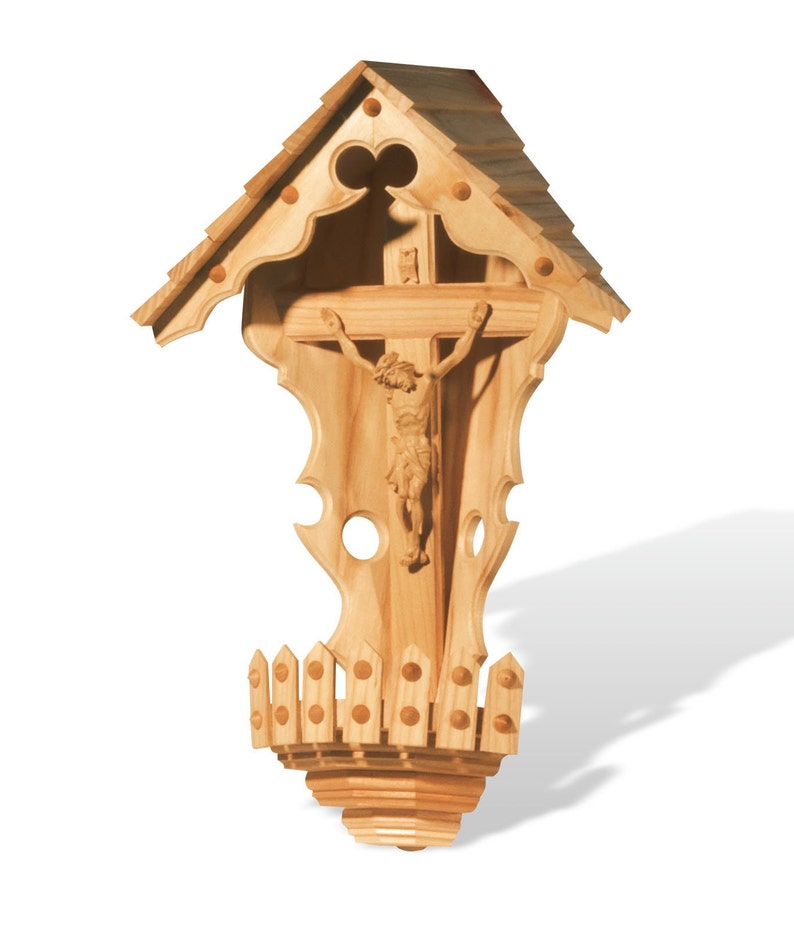 Puede incluir: Un crucifijo de madera para colgar en la pared con una figura tallada de Jesucristo. El crucifijo est&aacute; encerrado en un marco de madera decorativo con un techo y una base en forma de valla.