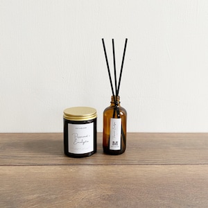 May include: A brown glass candle jar with a gold lid and a white label that reads "Mint & Bloom Peppermint + Eucalyptus" next to a brown glass diffuser bottle with black reeds and a white label that reads "Mint & Bloom  Peppermint Eucalyptus Diffuser".