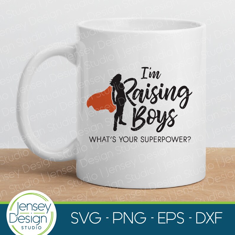 May include: White ceramic mug with a black silhouette of a woman wearing a red cape and the text "I'm Raising Boys" in black. The text "What's your superpower?" is also printed in black below the main text.