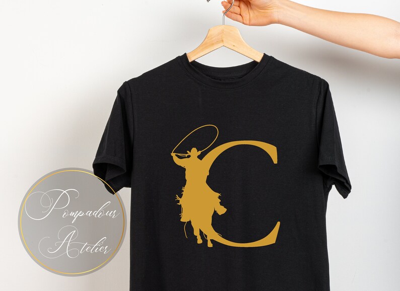May include: Black t-shirt with a gold silhouette of a cowboy riding a horse and lassoing a rope, forming the letter "C".