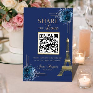 Könnte beinhalten: Ein marineblaues Hochzeitsschild mit goldenem Text, der "SHARE THE Love" lautet. Es zeigt einen QR-Code, eine Eiffelturm-Grafik und florale Akzente. Der Text "SHARE YOUR PHOTOS WITH ME! SCAN THE CODE AND UPLOAD" ist ebenfalls enthalten.