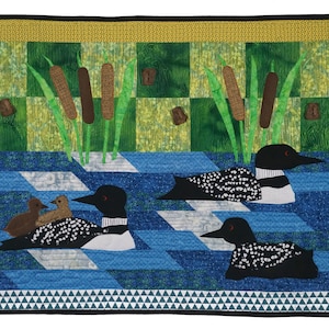 May include: A quilt depicting a family of loons swimming in a lake. The quilt features a blue and white checkered pattern for the water, green and brown reeds, and a yellow border.