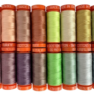 May include: A collection of 18 spools of Aurifil thread in various shades of orange, pink, purple, green, and gray. The spools are labeled with the brand name "Aurifil" and the text "100% Cotton - Made in Italy".