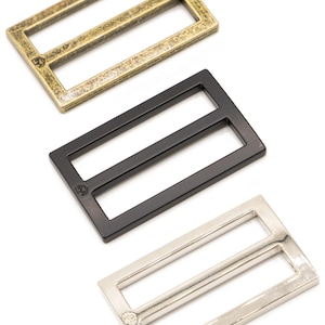 May include: Three metal rectangular sliders in antique brass, black, and silver. Each slider has a rectangular frame with two parallel bars. The antique brass slider has a textured finish, while the black and silver sliders have a smooth finish.