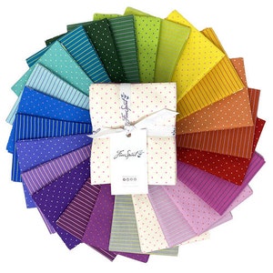 Puede incluir: Una colección de 24 cuadrados de tela en un arcoíris de colores, con varios patrones como lunares, rayas y lisos. Los cuadrados de tela están dispuestos en un círculo, con el texto "Free Spirit" impreso en una etiqueta blanca en el centro.