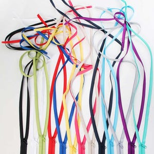 Può includere: Una collezione di cerniere colorate in varie tonalità, tra cui nero, bianco, rosso, giallo, blu, rosa e viola. Ogni cerniera ha un nastro abbinato che si estende dalla parte superiore. Le cerniere sono disposte su uno sfondo bianco.