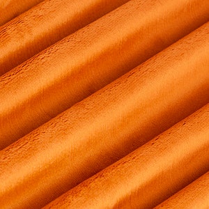 Puede incluir: Primer plano de una tela suave y naranja con una textura peluda. La tela está doblada en una serie de líneas paralelas, creando un efecto ondulado.