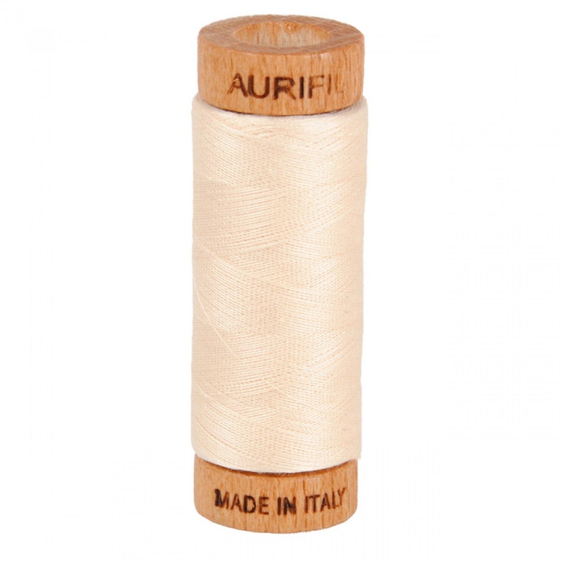 May include: A spool of cream-colored thread with wooden ends. The top end has the word "Aurifil" printed on it. The bottom end has the words "Made in Italy" printed on it.