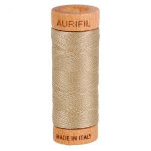 May include: A spool of Aurifil thread in a light beige color, wound on a wooden bobbin with the brand name "Aurifil" printed on the top and "Made in Italy" printed on the bottom.