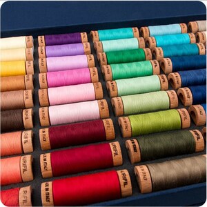 May include: A close-up of a wooden box filled with spools of colorful thread. The spools are labeled "Rifil" and "Made in Italy".